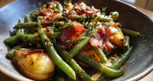 Nahaufnahme von Birnen, Bohnen und Speck, die sanft in einer schwarzen Gusseisenpfanne köcheln.