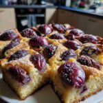Ein quadratisches Stück Zwetschgenkuchen auf einem weißen Teller, mit einem Klecks Schlagsahne daneben.