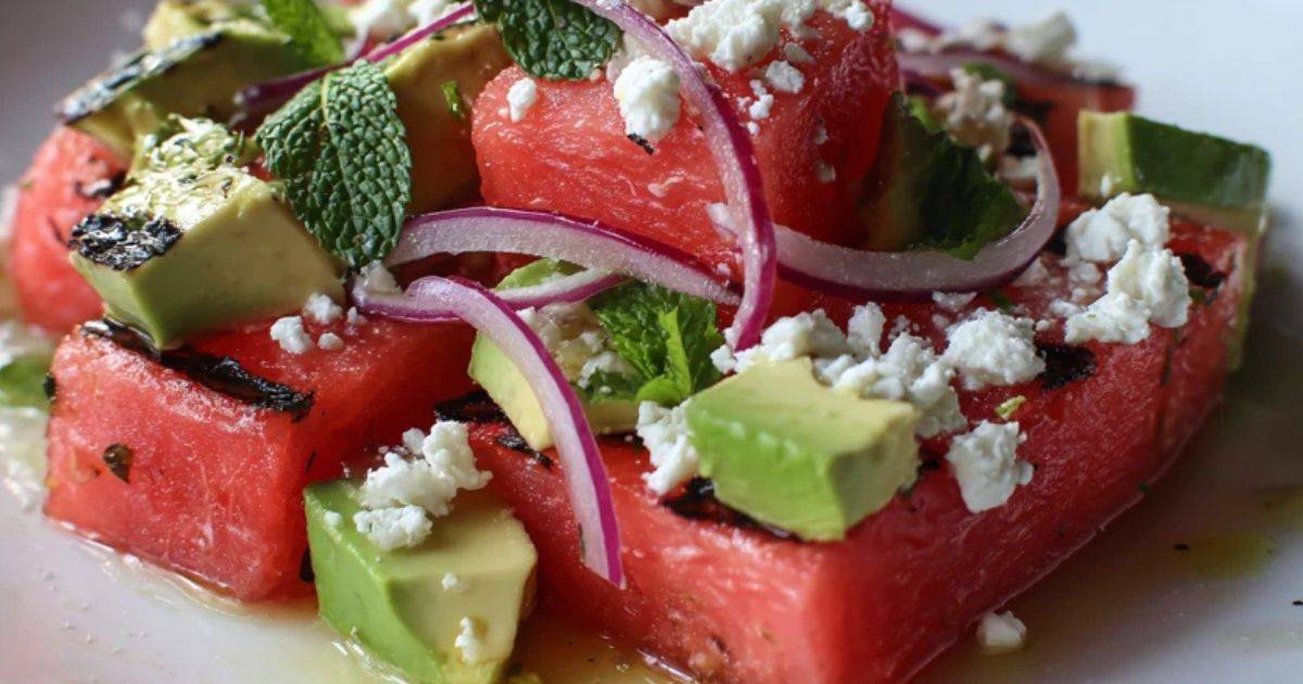 Een portie gegrilde watermeloensalade op een lichtblauw bord, klaar om gegeten te worden.