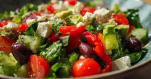 Een grote witte kom gevuld met een kleurrijke gehakte salade met feta, tomaat, komkommer en avocado.