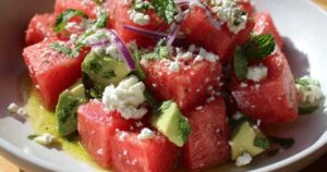 Gelaagde maaltijdsalade met sla, tomaat, komkommer, feta en ei in een glazen schaal.