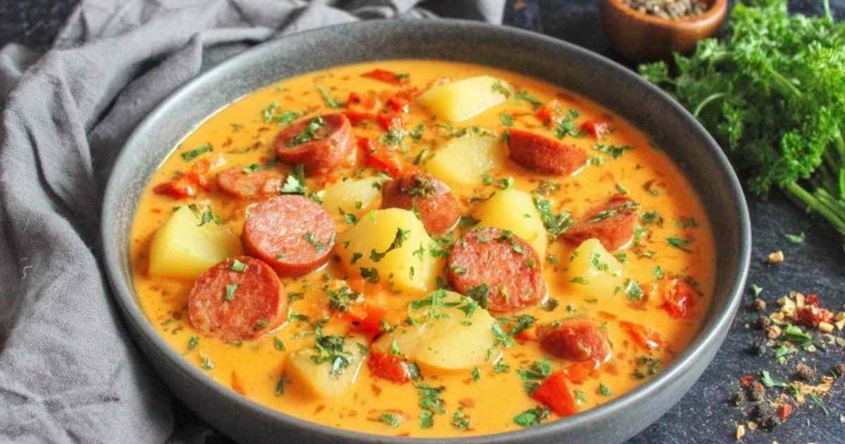 Kartoffelgulasch mit Würstchen in weißer Schüssel mit Petersilie garniert