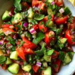 Een kleurrijke Shirazi salade in een witte keramische schaal, gegarneerd met een takje munt.