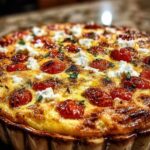 Een portie hartige clafoutis met feta op een bord, met de romige binnenkant en stukjes tomaat zichtbaar.