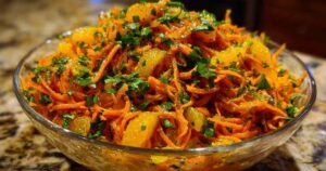 Een kom met feloranje wortelsalade met sinaasappel en komijn, gegarneerd met verse koriander.