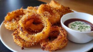 Air Fryer Zwiebel-Ringe goldbraun und knusprig auf weißem Teller angerichtet