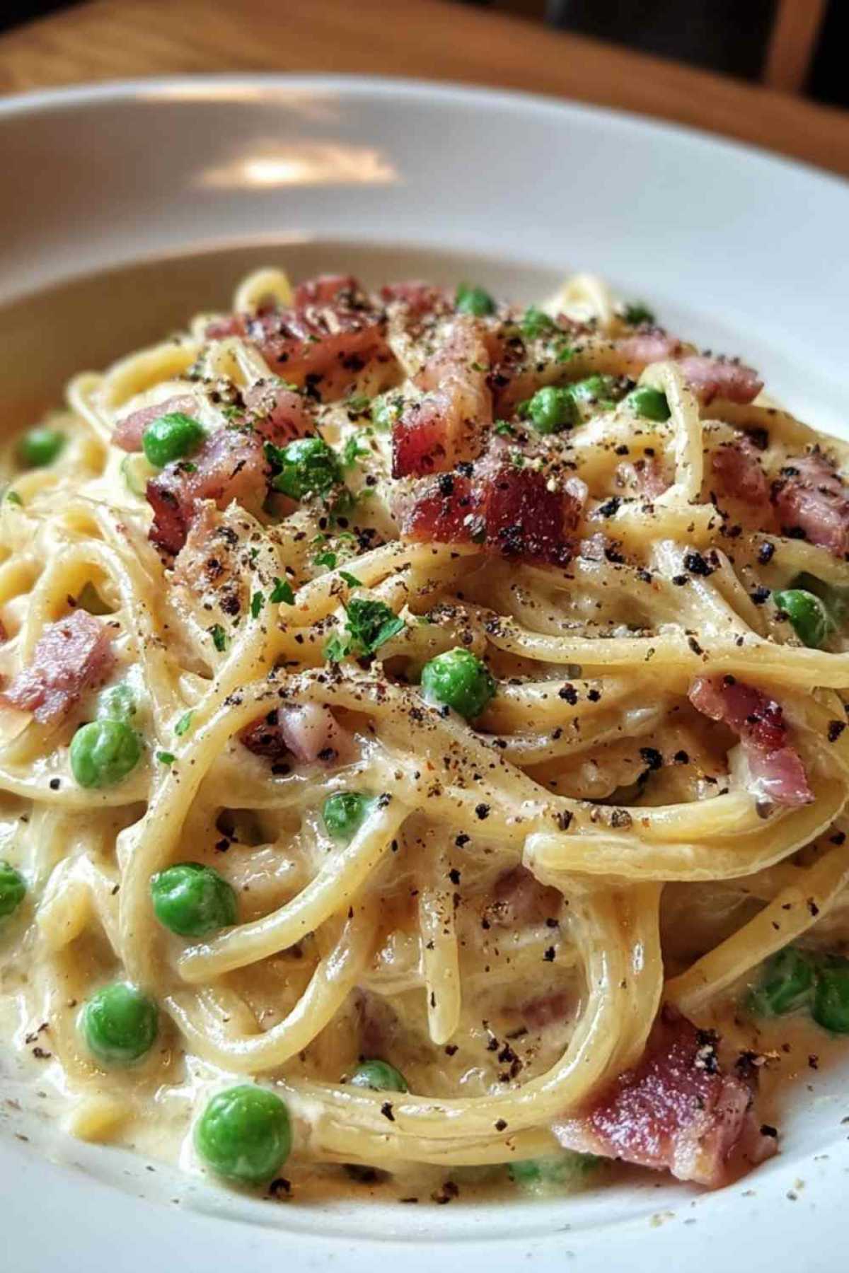 Cremige Speck-Erbsen-Carbonara in schwarzer Pfanne mit knusprigem Speck und grünen Erbsen