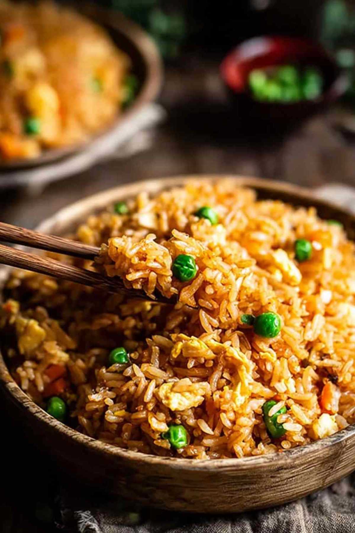 Gebratener Reis mit Gemüse und Ei in einer großen Pfanne mit Holzlöffel beim Kochen