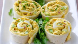 Kichererbsen-Salat-Röllchen aufgeschnitten auf Holzbrett zeigen cremige Füllung mit Spinat