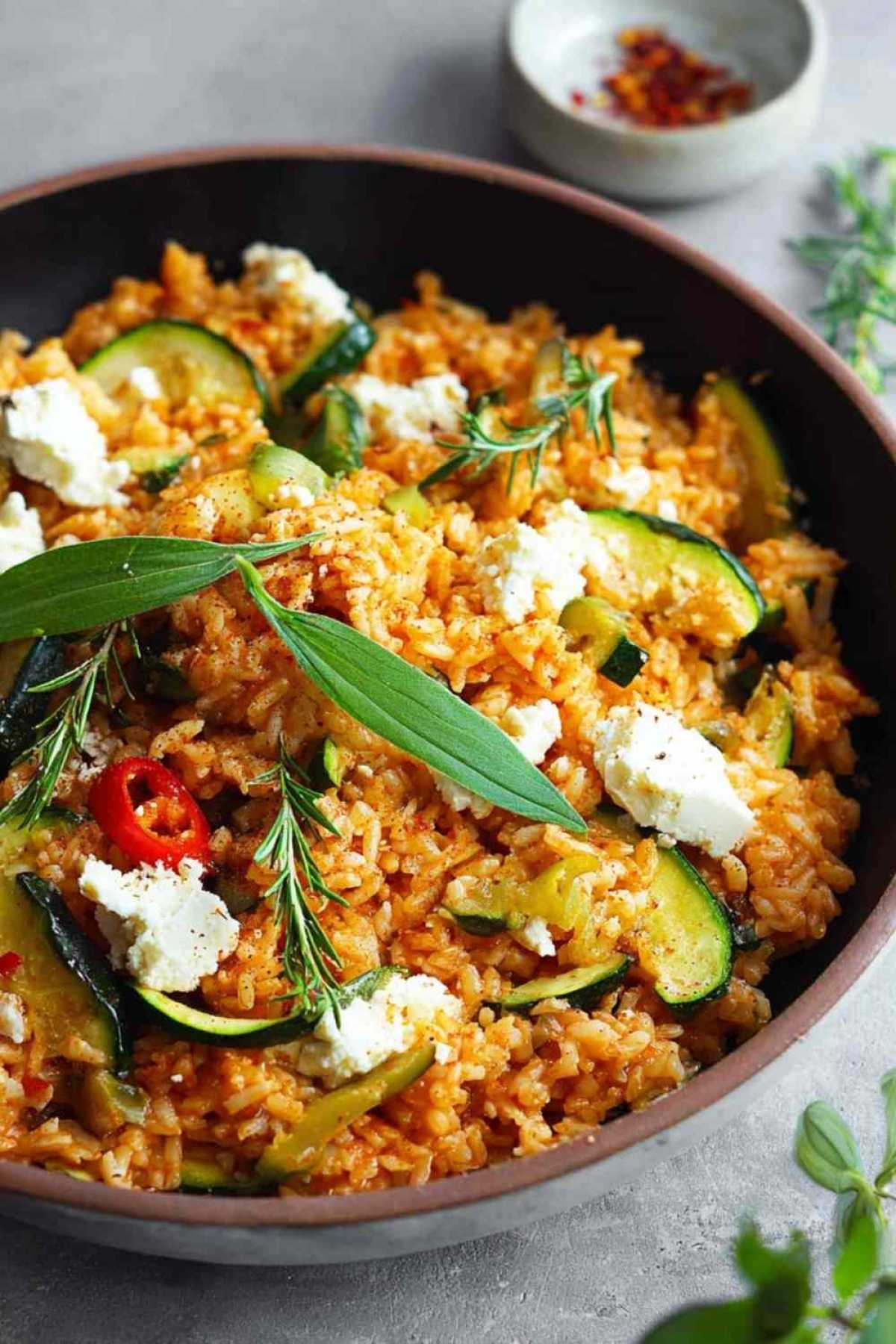 Mediterrane Zucchini-Reis-Pfanne mit geschmolzenem Feta und frischen Kräutern in schwarzer Pfanne