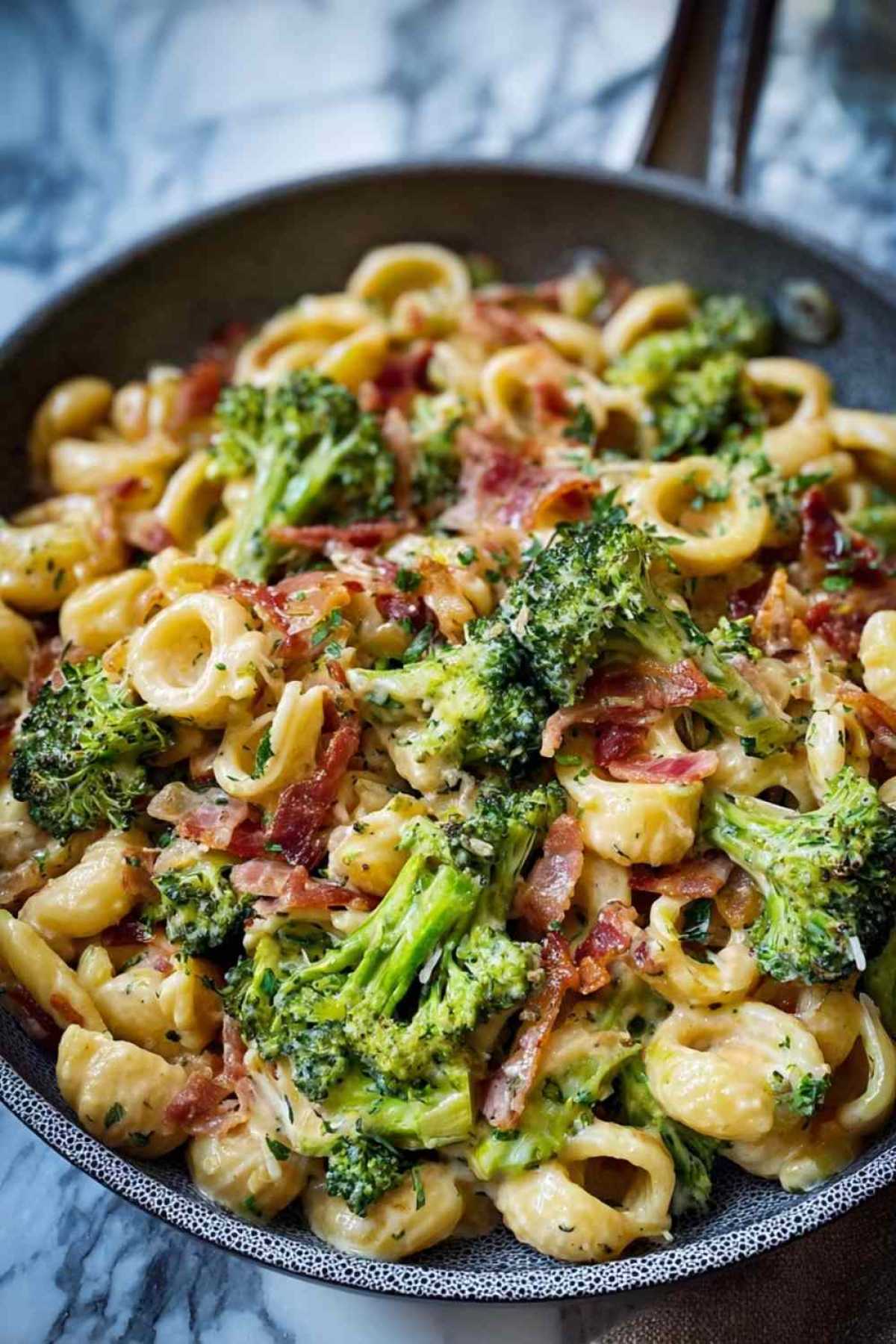 Cremige Pasta mit Brokkoli und Speck in großer Pfanne mit goldbraunen Champignons