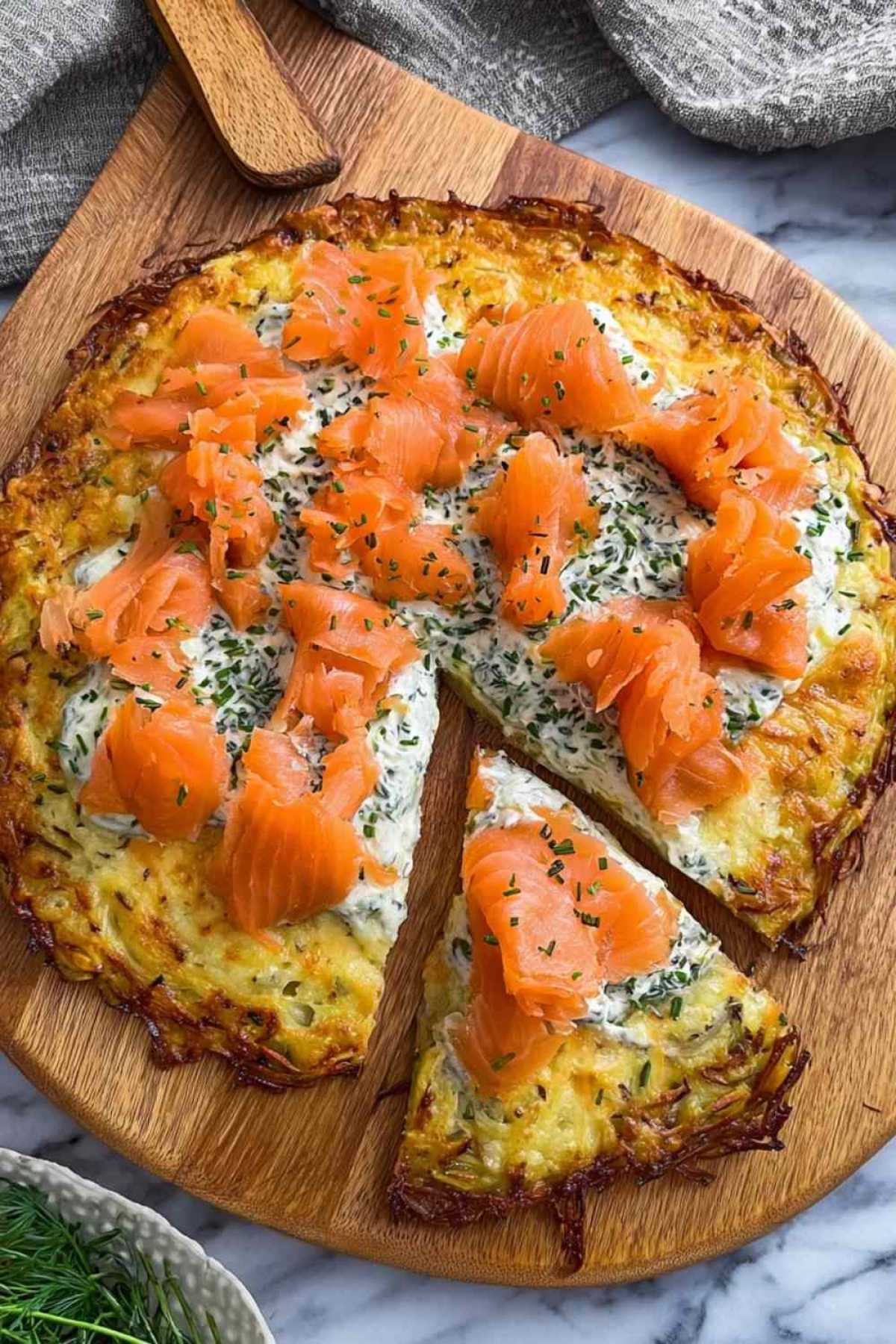 Kartoffelpizza mit geräuchertem Lachs und Kräuterfrischkäse auf Backpapier mit frischem Dill garniert