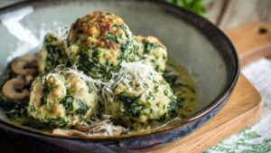 Spinatknödel als Hauptgericht mit cremiger Champignonsoße auf weißem Teller serviert