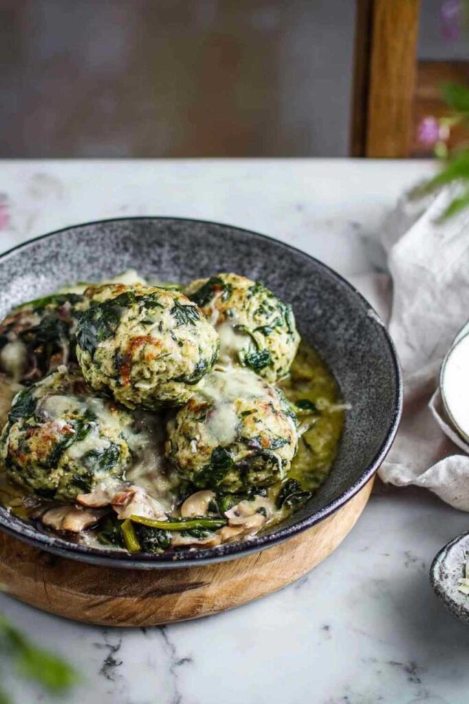Spinatknödel als Hauptgericht mit cremiger Champignonsoße auf weißem Teller serviert