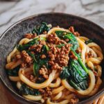 Udon-Nudeln mit Rinderhack und frischem Spinat in einer großen Pfanne beim Kochen