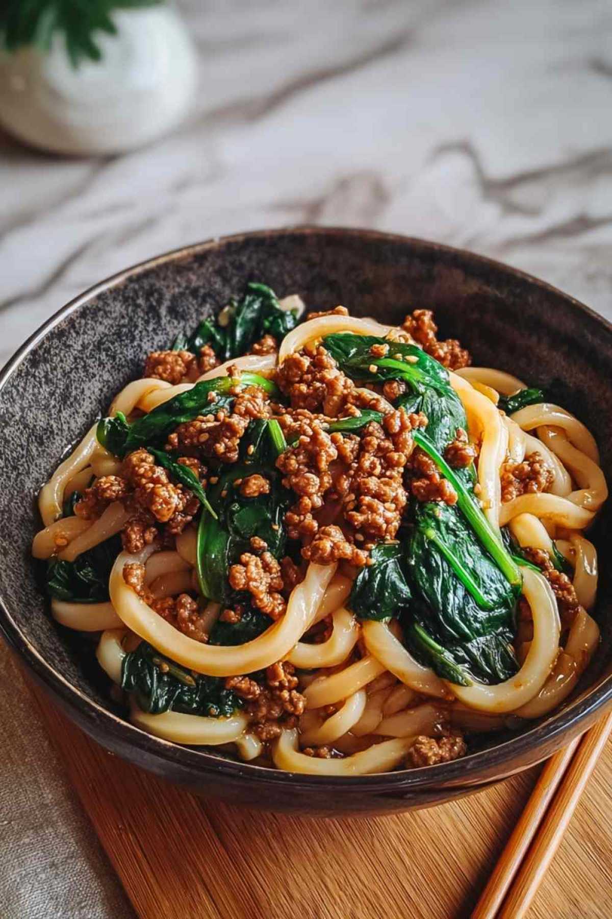 Udon-Nudeln mit Rinderhack und frischem Spinat in einer großen Pfanne beim Kochen