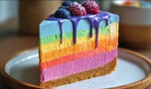 No bake Regenbogen-Käsekuchen mit bunten cremigen Schichten auf weißem Teller