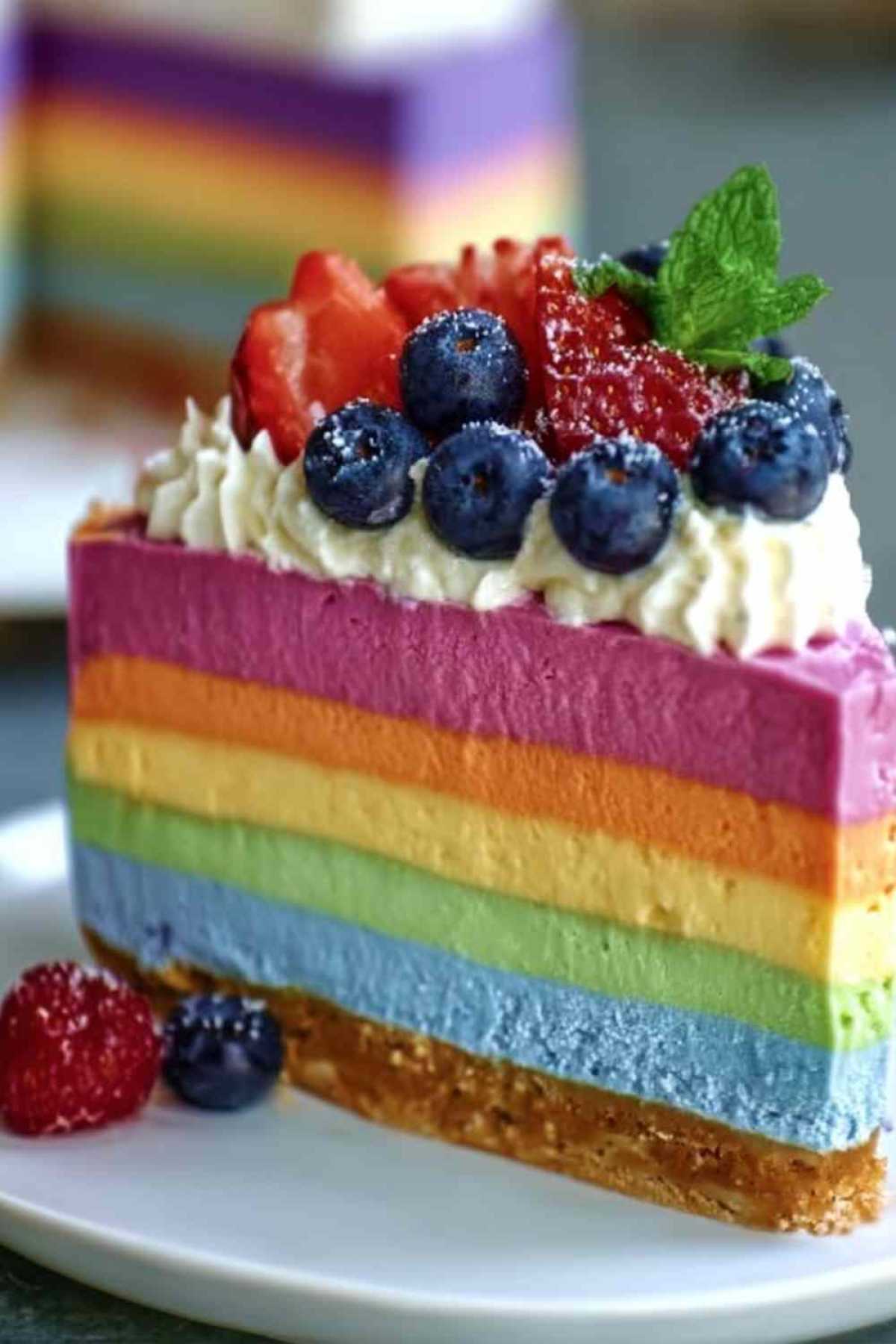 No bake Regenbogen-Käsekuchen mit bunten cremigen Schichten auf weißem Teller