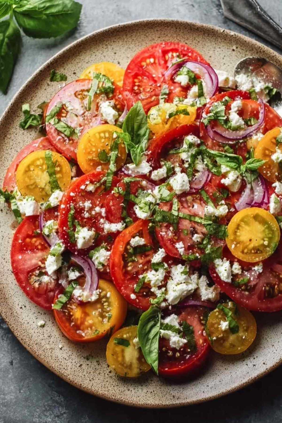 Tomaten-Feta-Salat mit Basilikum in weißer Schüssel servierfertig angerichtet