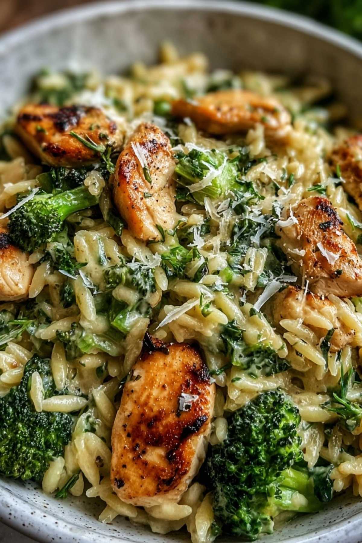 Portion cremiges Hähnchen-Brokkoli-Orzo auf weißem Teller garniert mit Petersilie