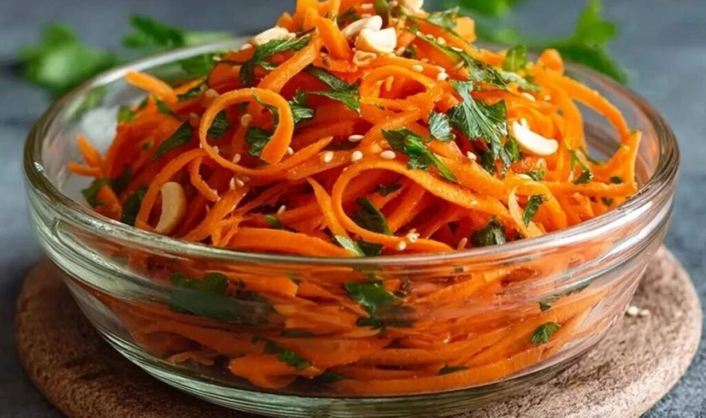 Koreanischer Karottensalat in weißer Schüssel mit Sesam garniert auf Holztisch