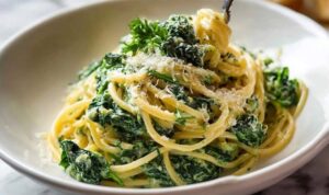 Spaghetti mit Spinat Frischkäse-Sauce auf weißem Teller mit frischem Parmesan garniert
